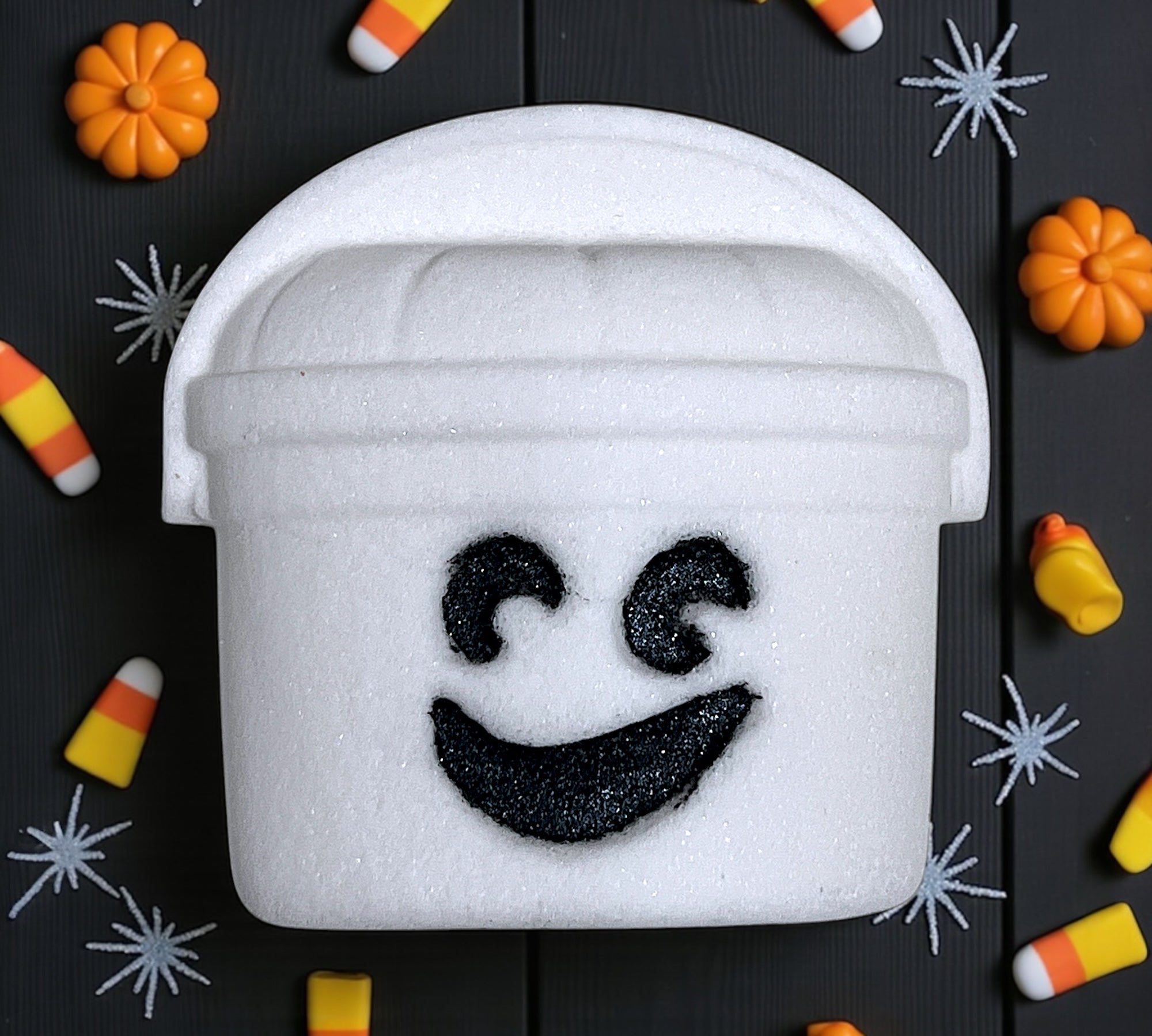 White foam bucket with ghost face design on a Halloween-themed background with pumpkins and candy corn.